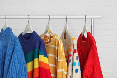 Collection of warm sweaters hanging on rack against white brick wall