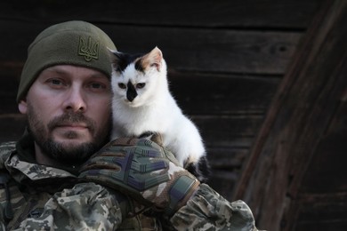Photo of Ukrainian soldier rescuing animal. Little stray cat on man's shoulder, closeup. Space for text