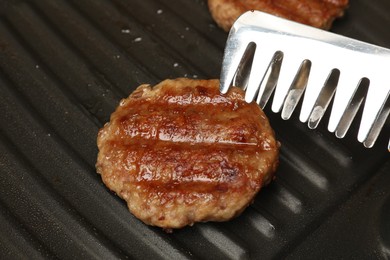 Taking delicious hamburger patty with tongs from grill pan, closeup