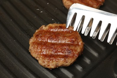 Photo of Taking delicious hamburger patty with tongs from grill pan, closeup