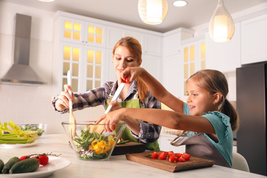 Photo of Mother and daughter cooking salad together in kitchen