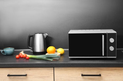 Modern microwave oven and ingredients on table in kitchen