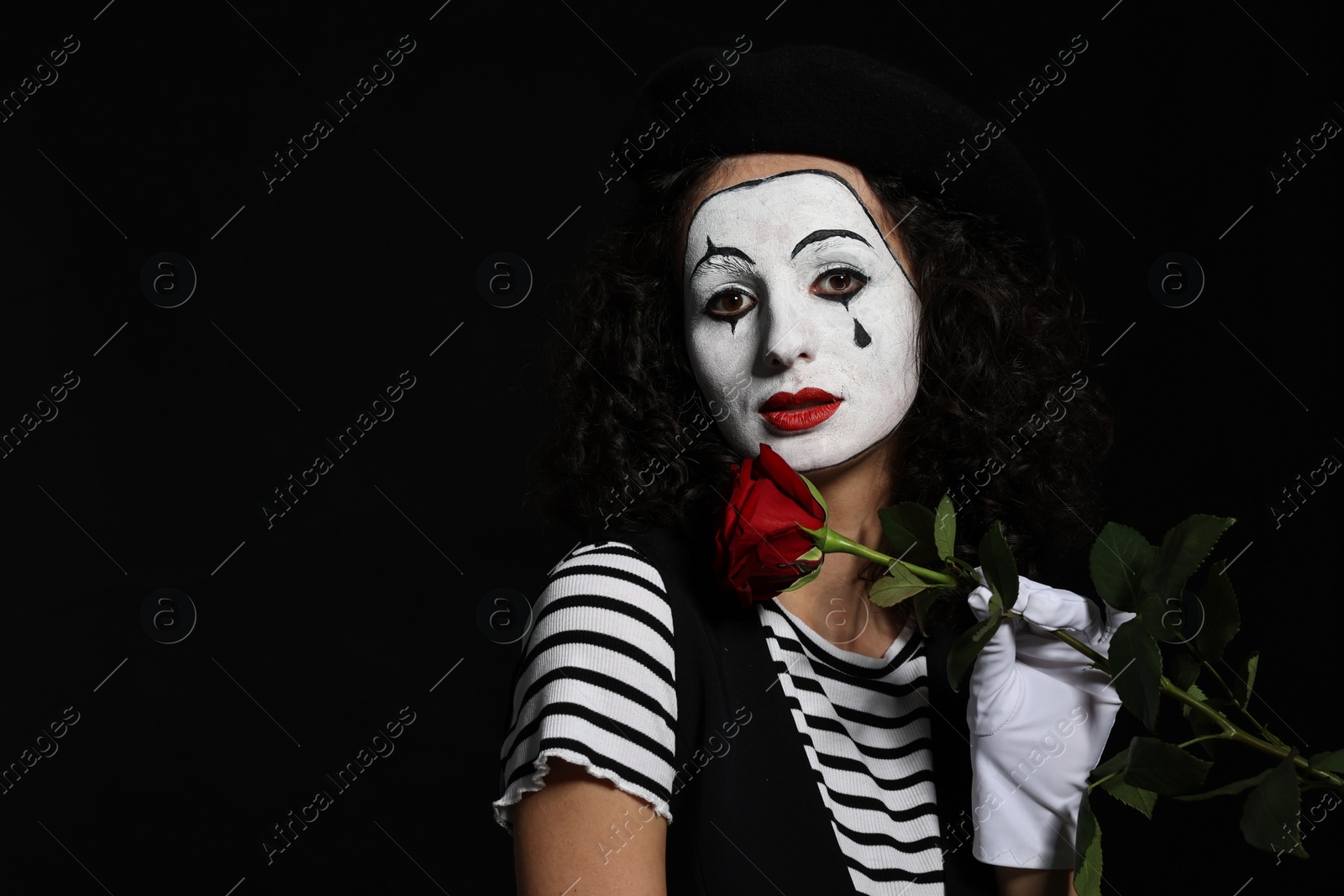 Photo of Young woman in mime costume with red rose posing on black background, space for text