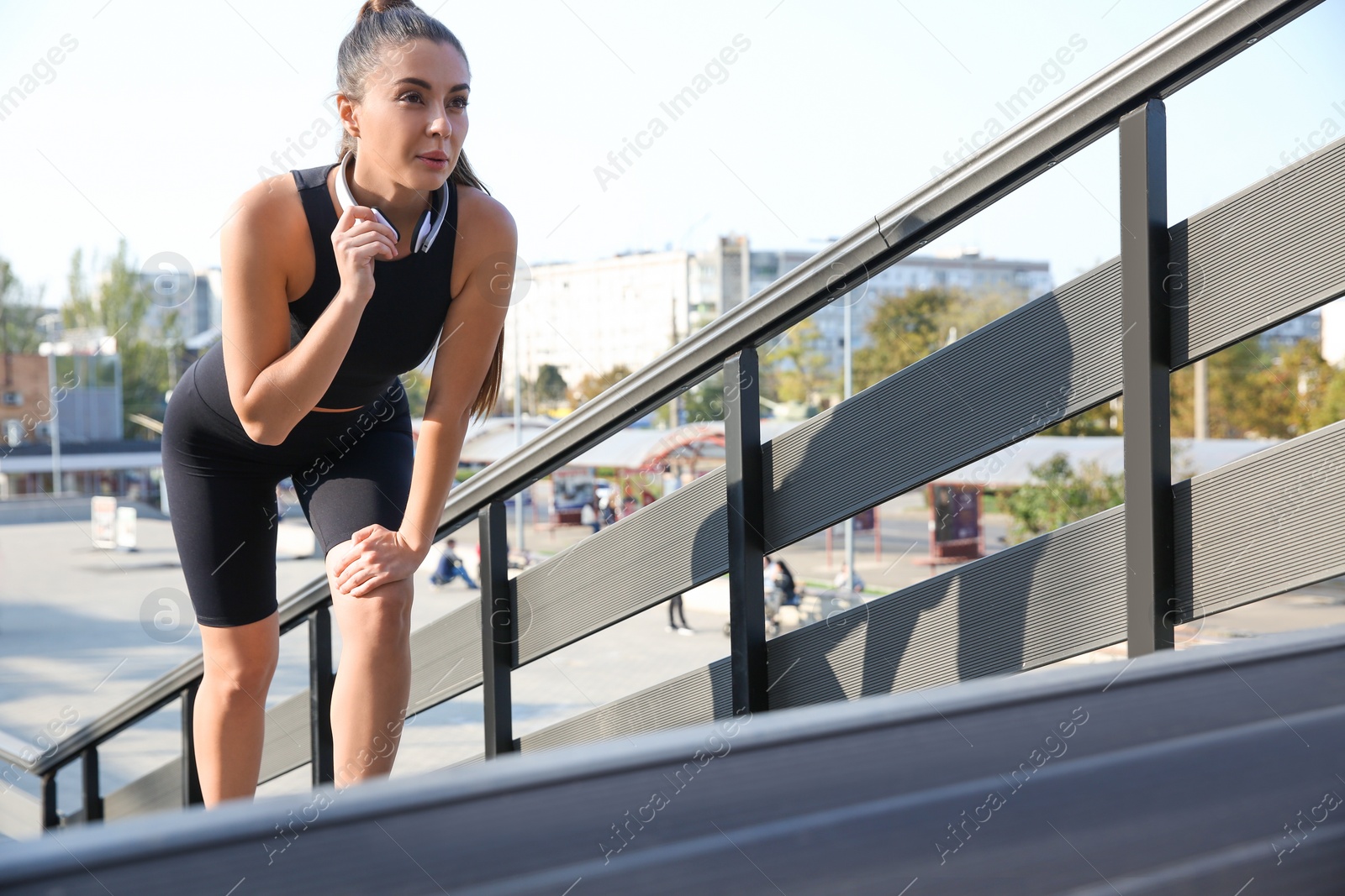 Photo of Young woman in sportswear with headphones on stairs outdoors. Space for text