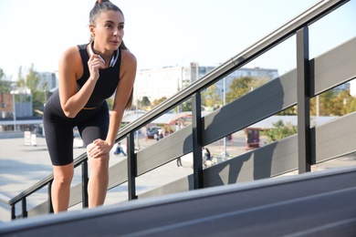 Young woman in sportswear with headphones on stairs outdoors. Space for text