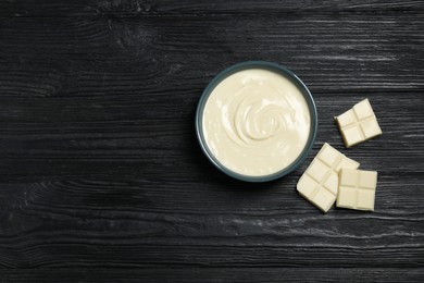 Photo of Tasty white chocolate paste in bowl and pieces on black wooden table, top view. Space for text