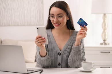 Woman with credit card using smartphone for online shopping at white table indoors