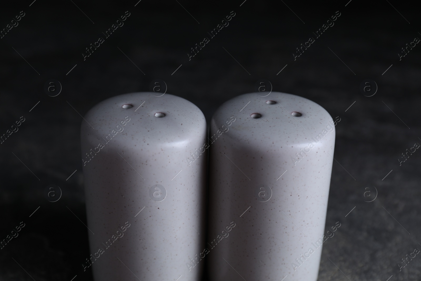 Photo of Salt and pepper shakers on dark table, closeup