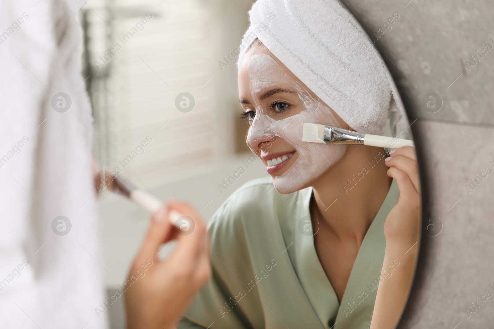 Photo of Woman applying face mask in front of mirror indoors. Spa treatments