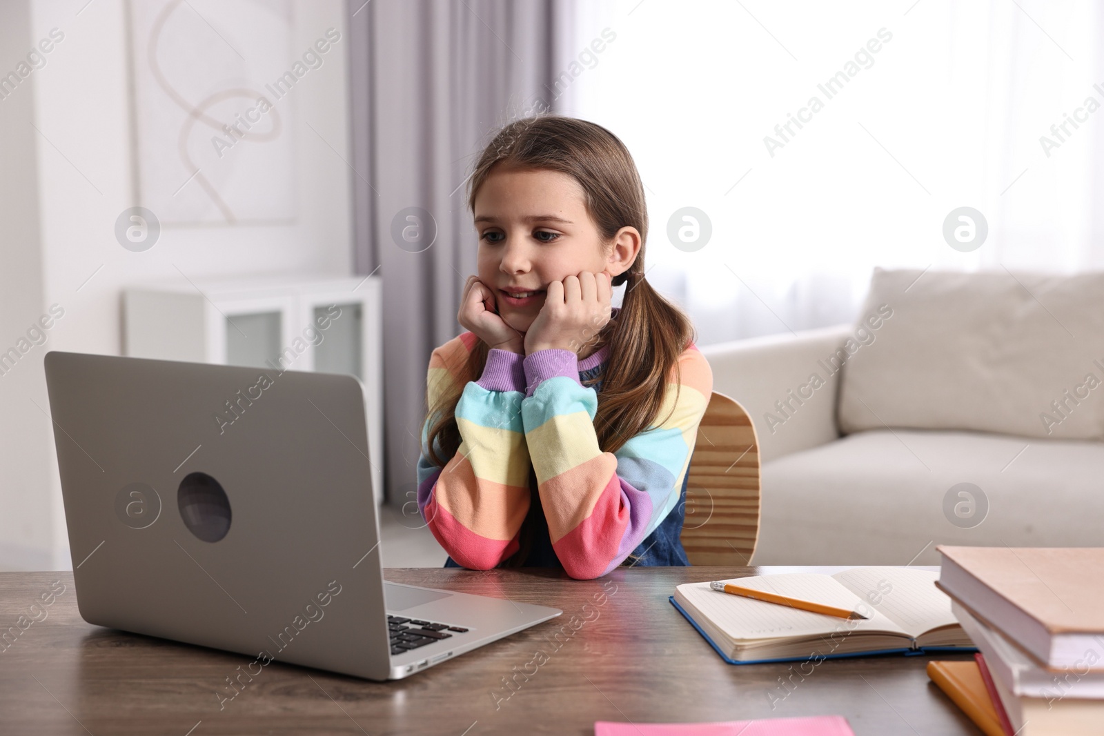 Photo of E-learning. Cute girl using laptop during online lesson at table indoors