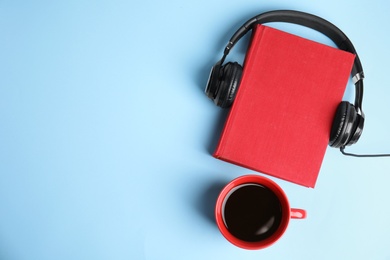 Photo of Modern headphones with hardcover book and coffee on light blue background, top view. Space for text