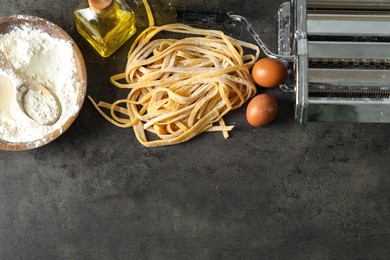 Homemade pasta, maker and ingredients on dark grey table, flat lay. Space for text