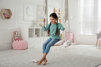 Cute little girl playing on swing at home