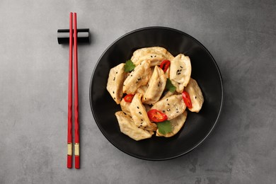 Delicious gyoza (asian dumplings) in bowl and chopsticks on gray table, flat lay