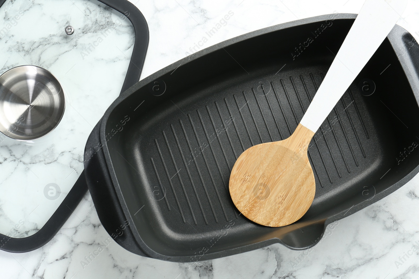 Photo of Black pot with glass lid and round spatula on white marble table, flat lay