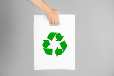 Woman holding bag with recycling symbol on grey background, closeup
