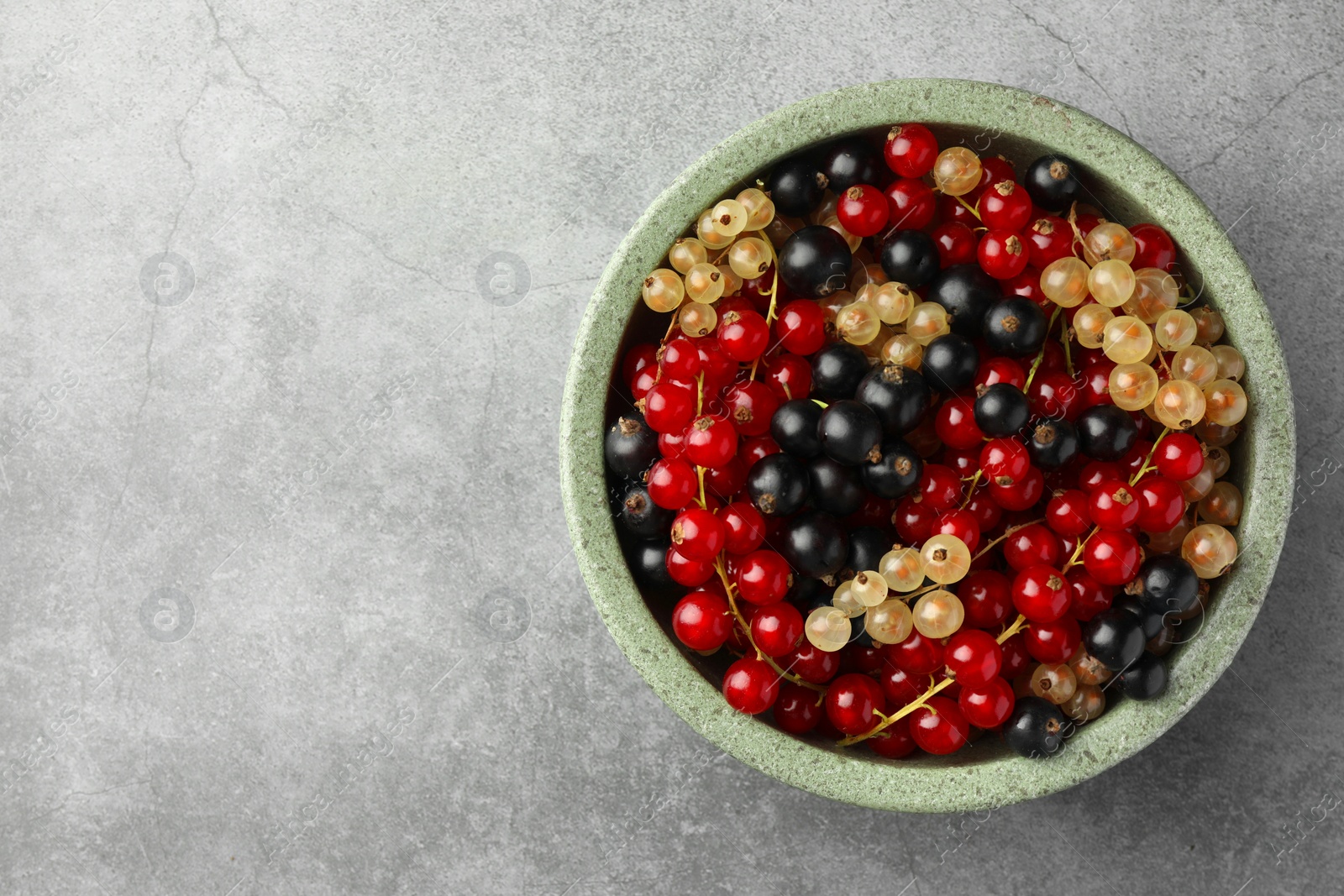 Photo of Different fresh ripe currants in bowl on light grey table, top view. Space for text