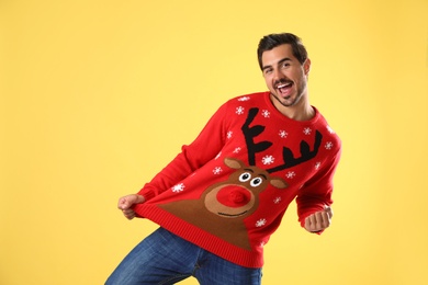 Photo of Portrait of happy young man in Christmas sweater on yellow background