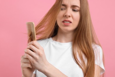 Photo of Emotional woman brushing her hair on pink background, selective focus. Alopecia problem