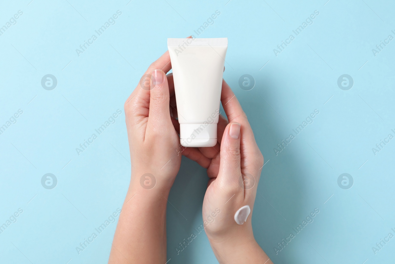 Photo of Woman with tube of hand cream on light blue background, top view