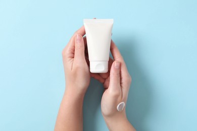 Photo of Woman with tube of hand cream on light blue background, top view