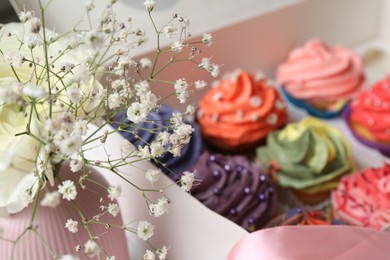 Photo of Different colorful cupcakes in box and flowers on table, closeup