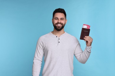 Photo of Smiling man with passport and tickets on light blue background