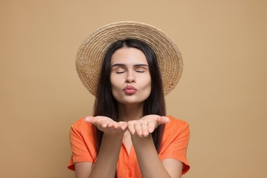 Photo of Beautiful young woman in straw hat blowing kiss on beige background