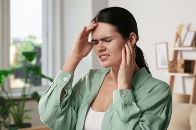 Young woman suffering from ear pain at home