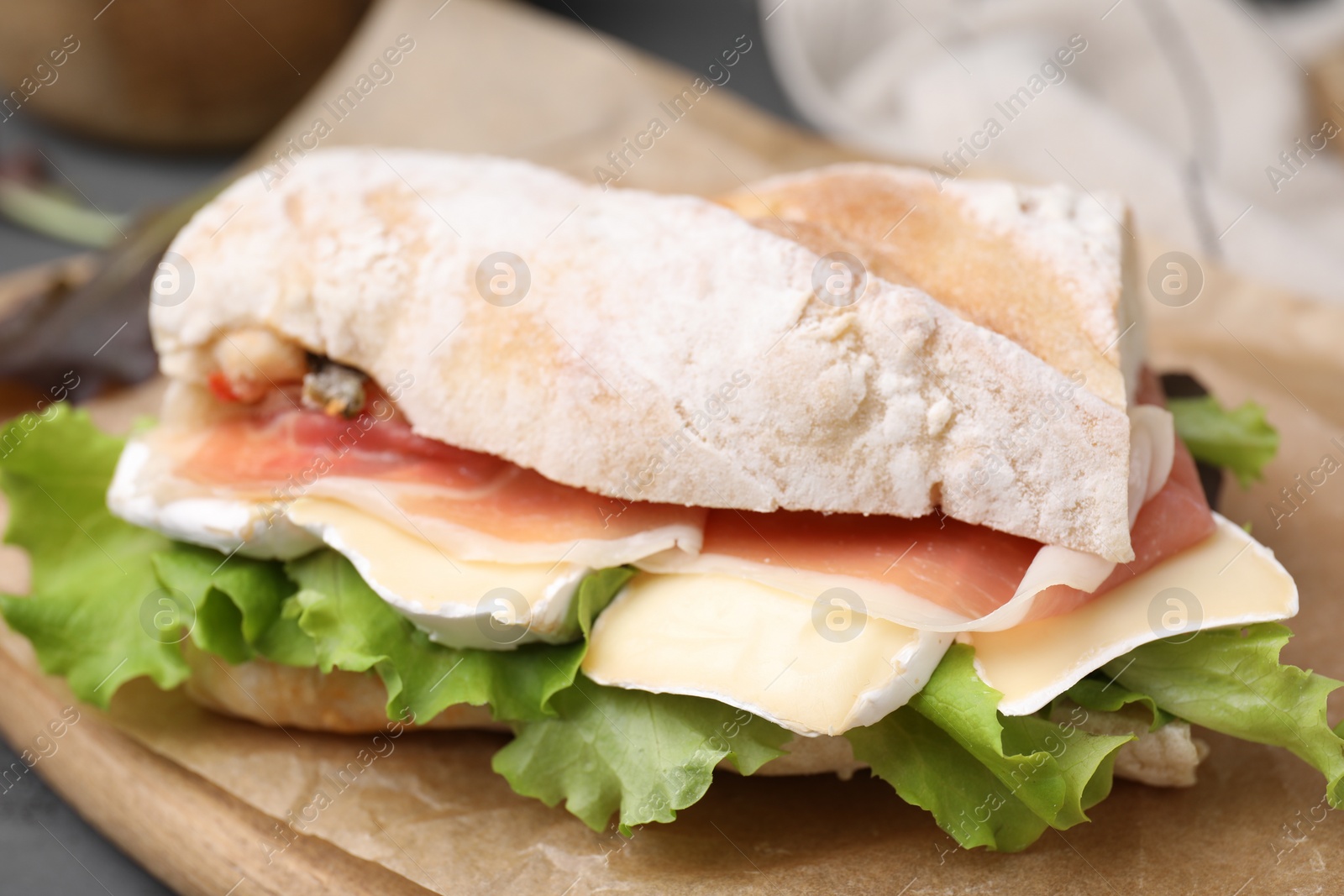 Photo of Tasty sandwich with brie cheese and prosciutto on board, closeup