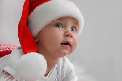 Cute baby in Santa hat on light grey background, closeup. Christmas celebration