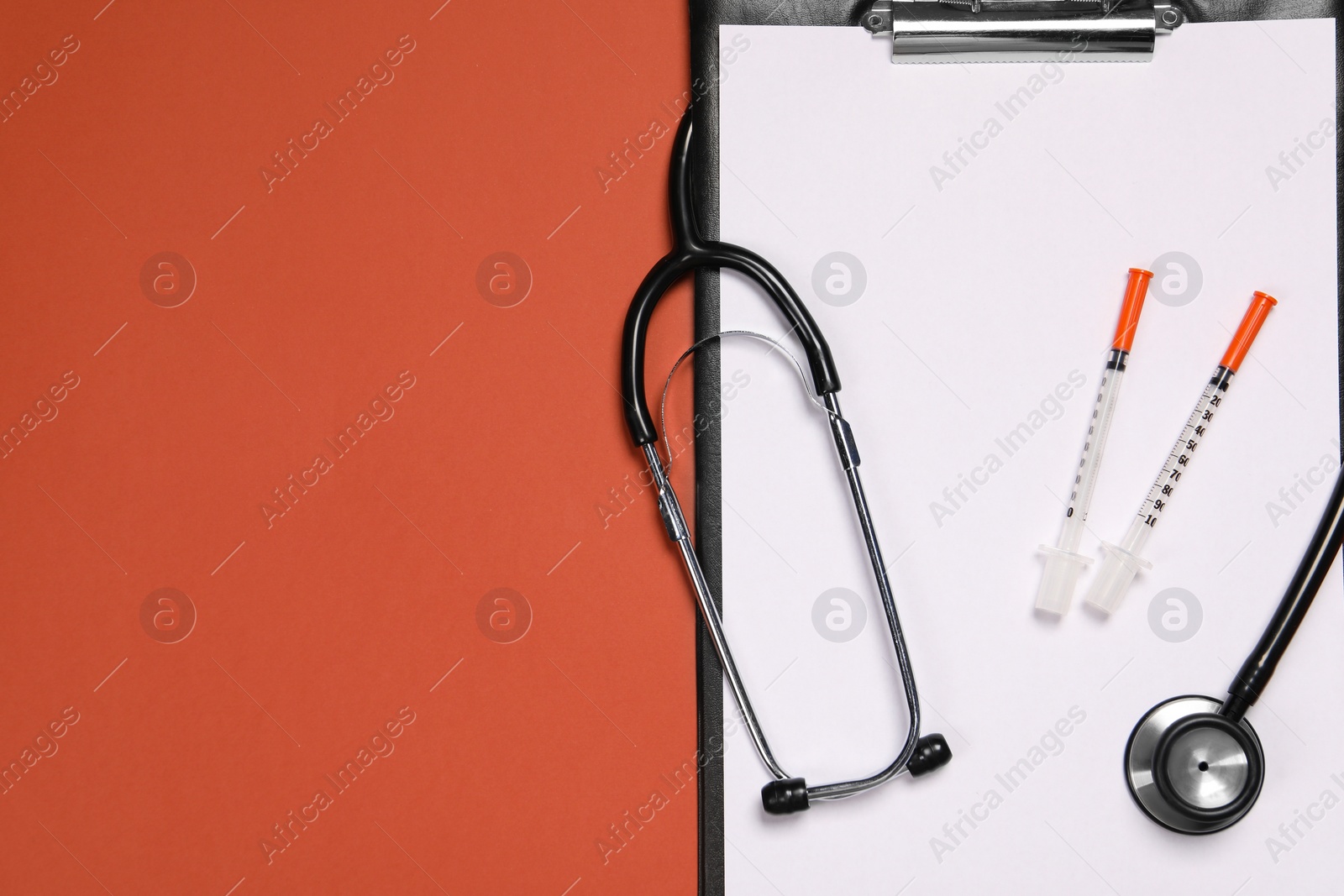 Photo of Stethoscope, syringes and clipboard on crimson background, top view. Space for text