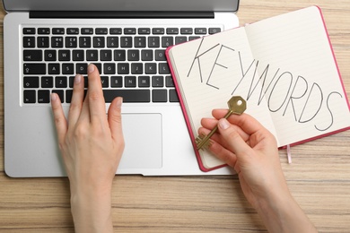 Woman with key working with laptop at wooden table, top view. Keyword concept