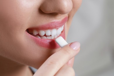 Photo of Woman putting chewing gum piece into mouth on blurred background, closeup. Space for text