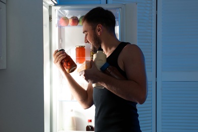 Photo of Man taking products out of refrigerator in kitchen at night