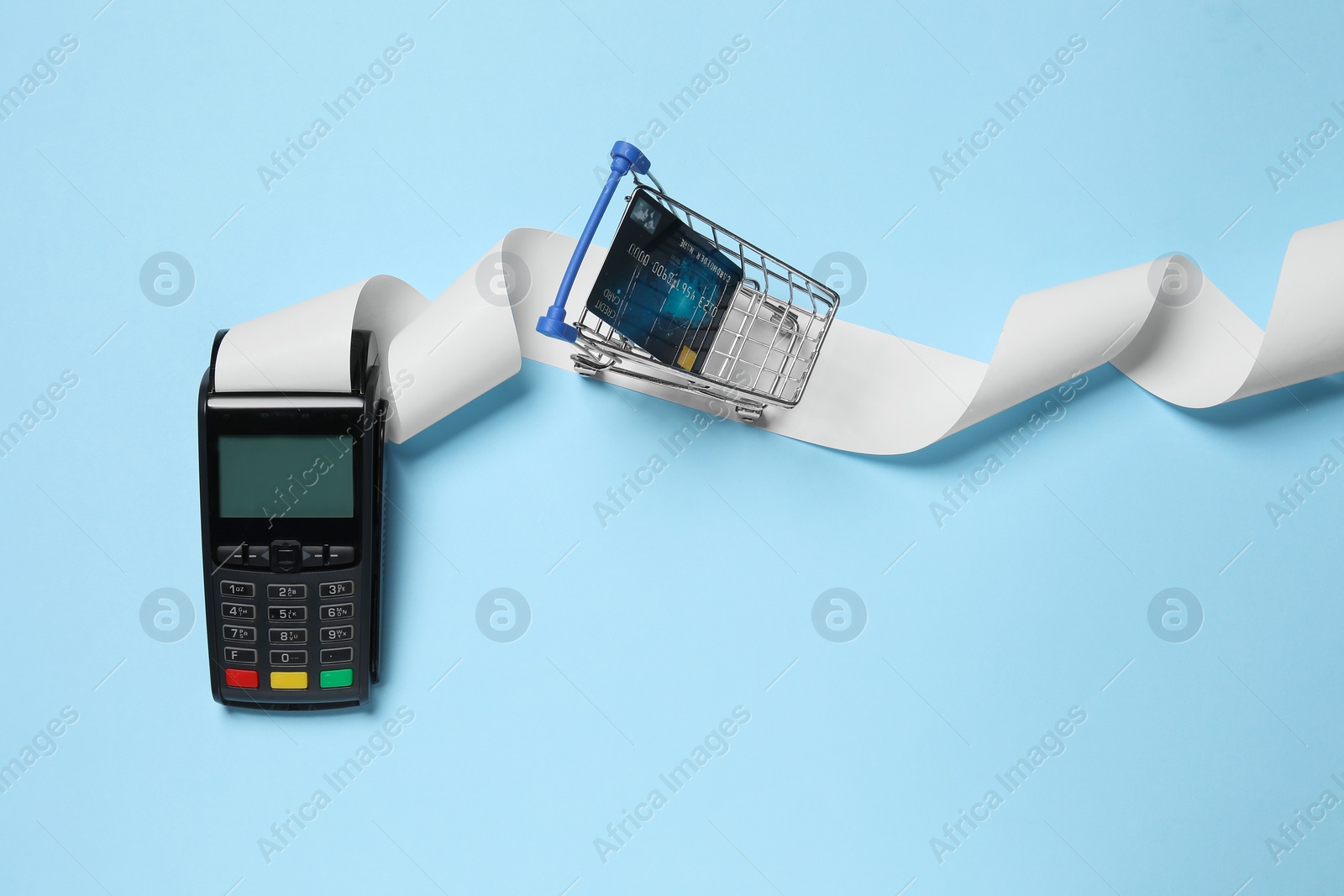 Photo of Payment terminal with thermal paper for receipt, small shopping cart and credit card on light blue background, flat lay