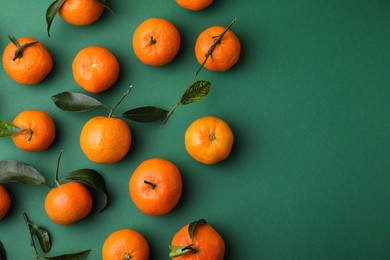 Photo of Fresh ripe tangerines with leaves on green background, flat lay. Space for text