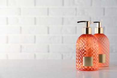 Photo of Stylish dispensers with liquid soap on wooden table near white brick wall, space for text