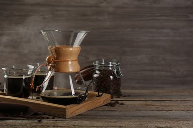 Glass chemex coffeemaker with coffee and beans on wooden table. Space for text
