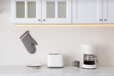 Photo of Modern toaster, coffeemaker and dishware on counter in kitchen