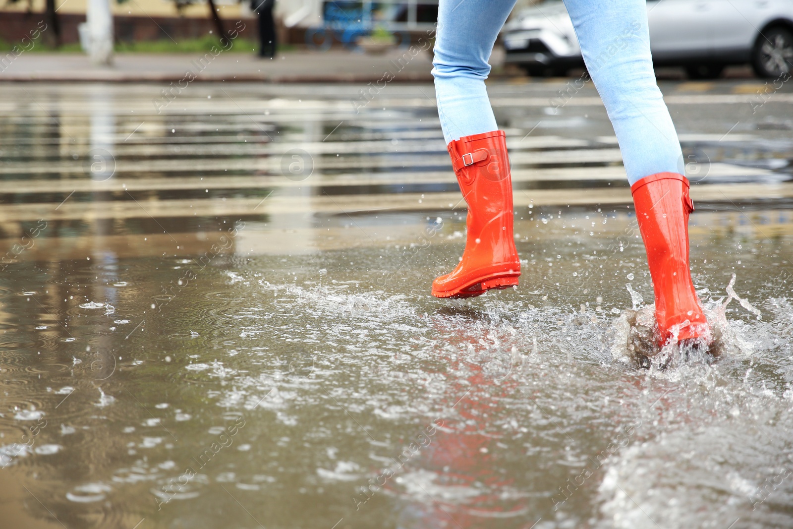 Photo of Woman with red rubber boots running in puddle, closeup. Rainy weather