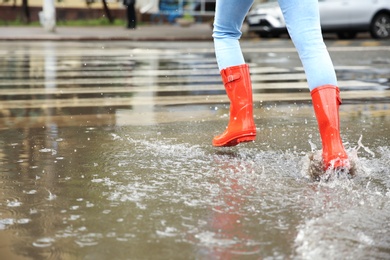 Woman with red rubber boots running in puddle, closeup. Rainy weather