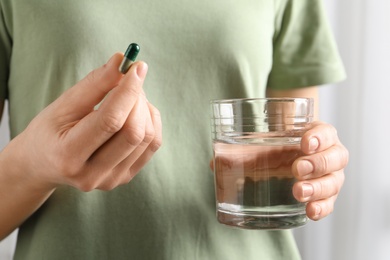 Photo of Woman holding spirulina pill and glass of water, closeup