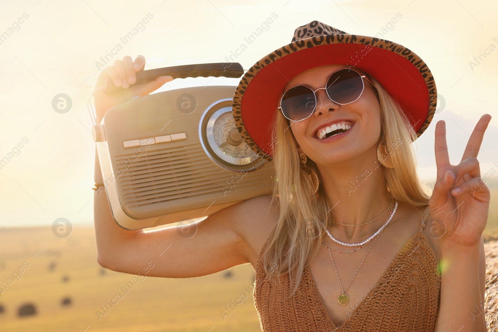 Photo of Happy hippie woman with radio receiver showing peace sign in field
