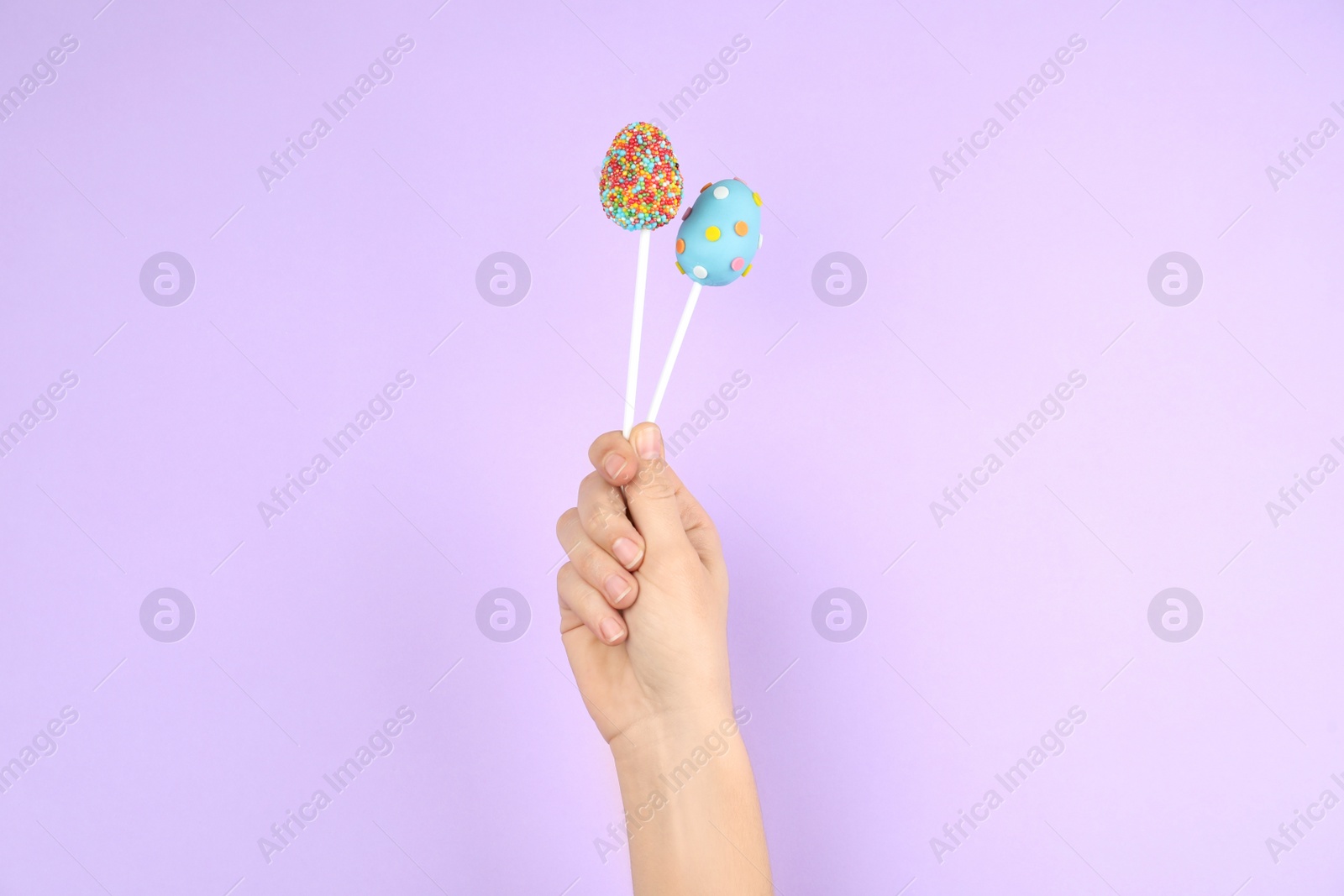 Photo of Woman with delicious cake pops on light pink background, closeup. Easter holiday