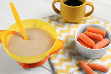 Photo of Baby food. Puree in bowl, small carrots and drink on white wooden table
