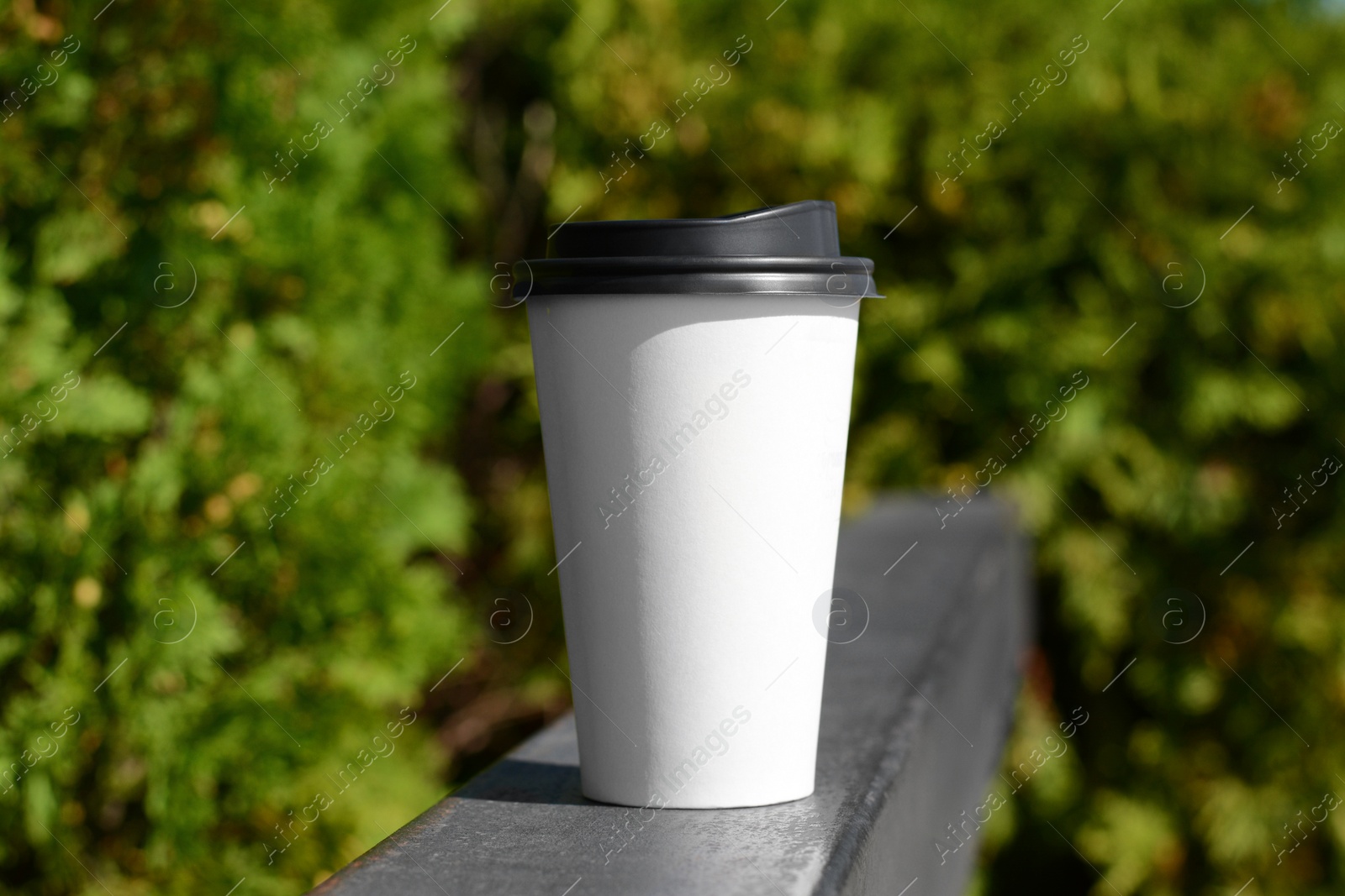 Photo of Takeaway coffee cup on metal railing outdoors. Space for text