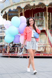Photo of Attractive young woman with color balloons near carousel