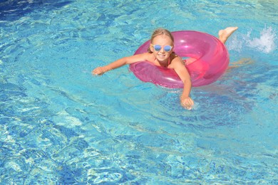 Photo of Cute little girl with inflatable ring in pool on sunny day. space for text