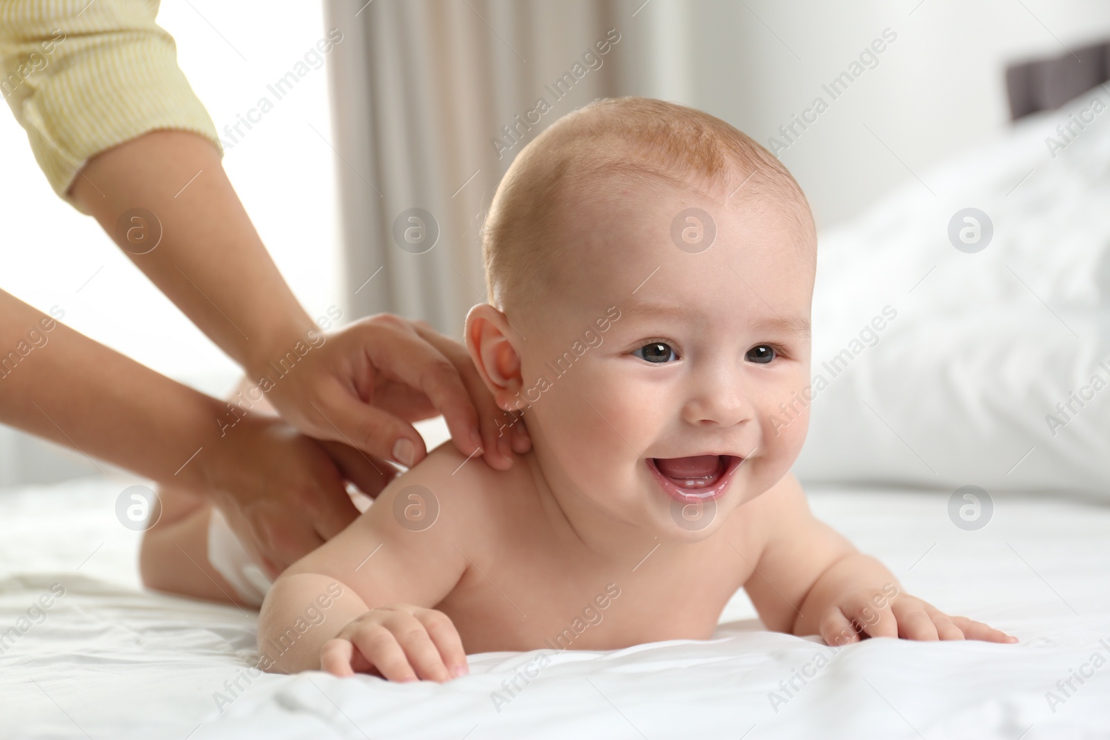 Photo of Young woman massaging cute little baby on bed indoors